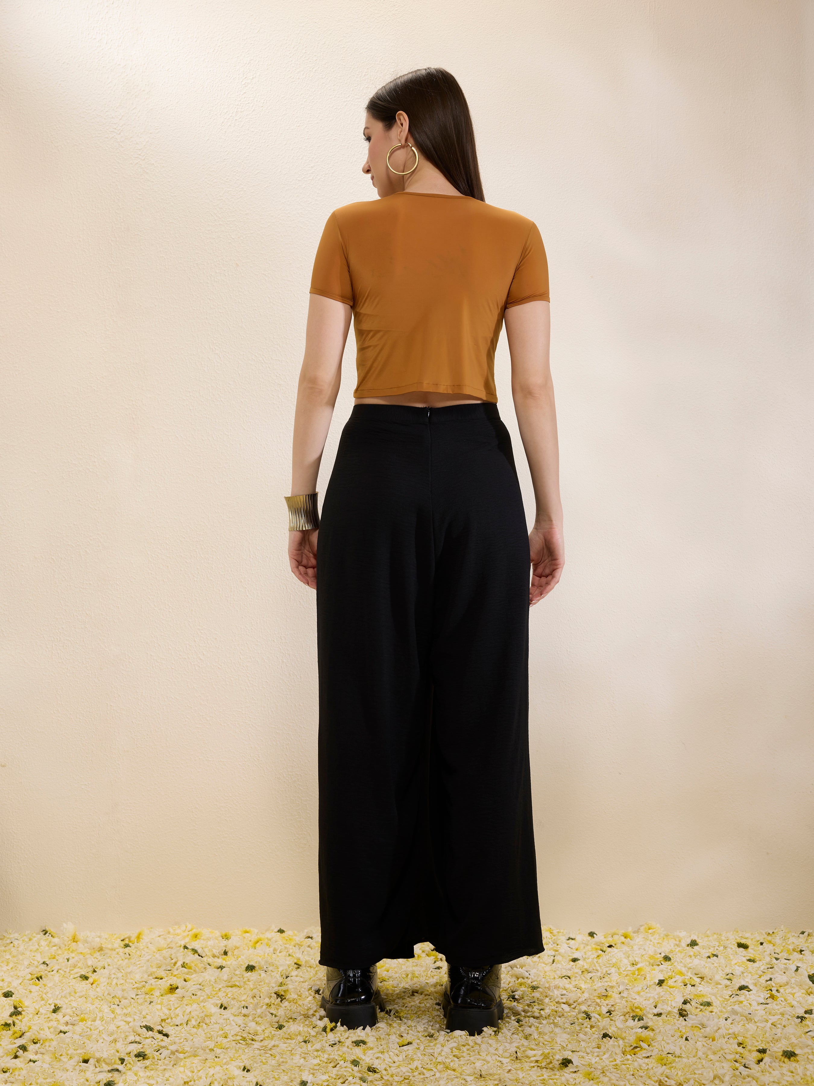 Woman wearing a mustard top and black pants standing on a textured surface with a neutral background