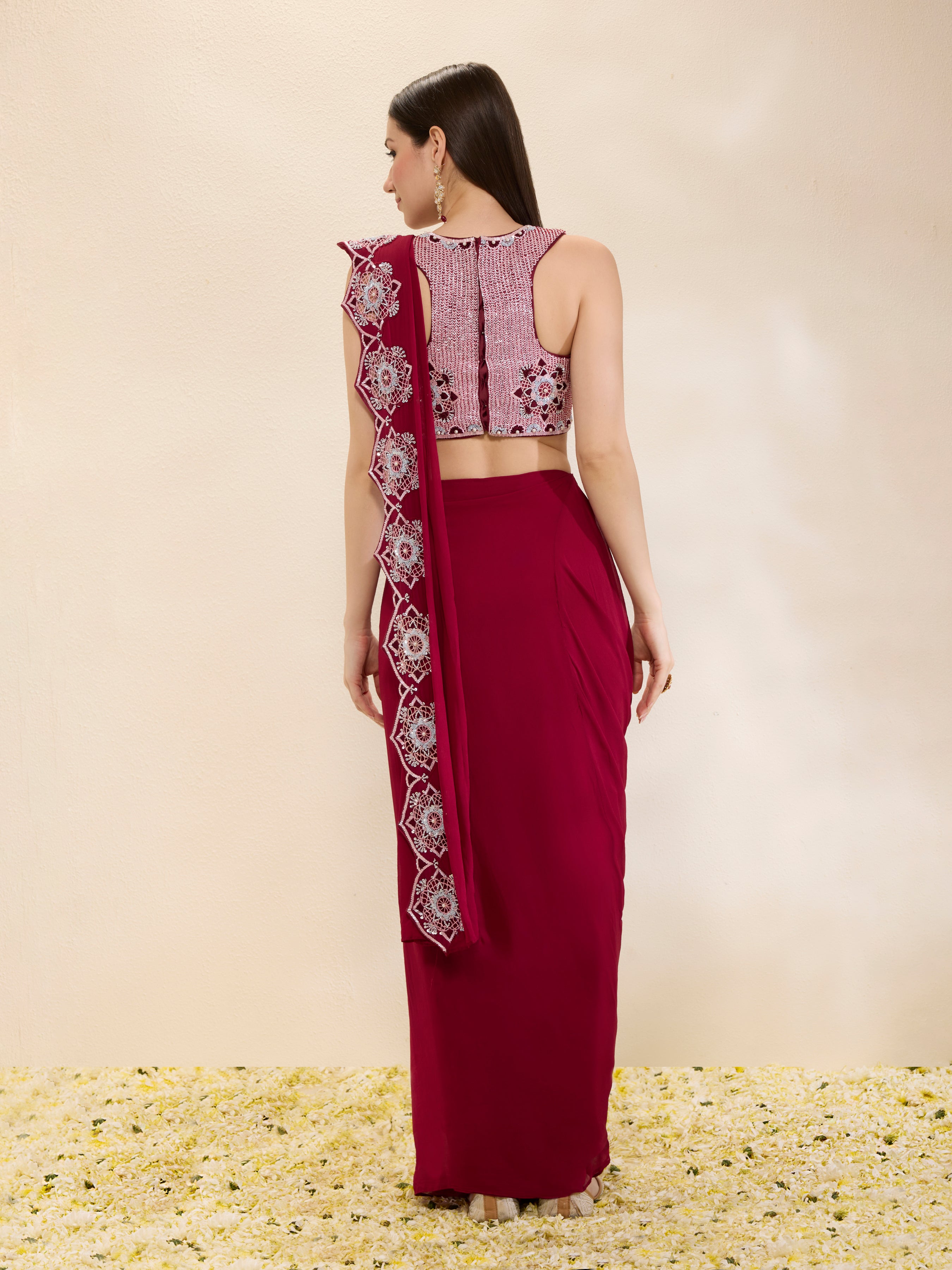 Woman wearing a maroon saree with a matching blouse against a beige background