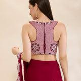 Woman wearing a maroon saree with an embroidered blouse on a beige background