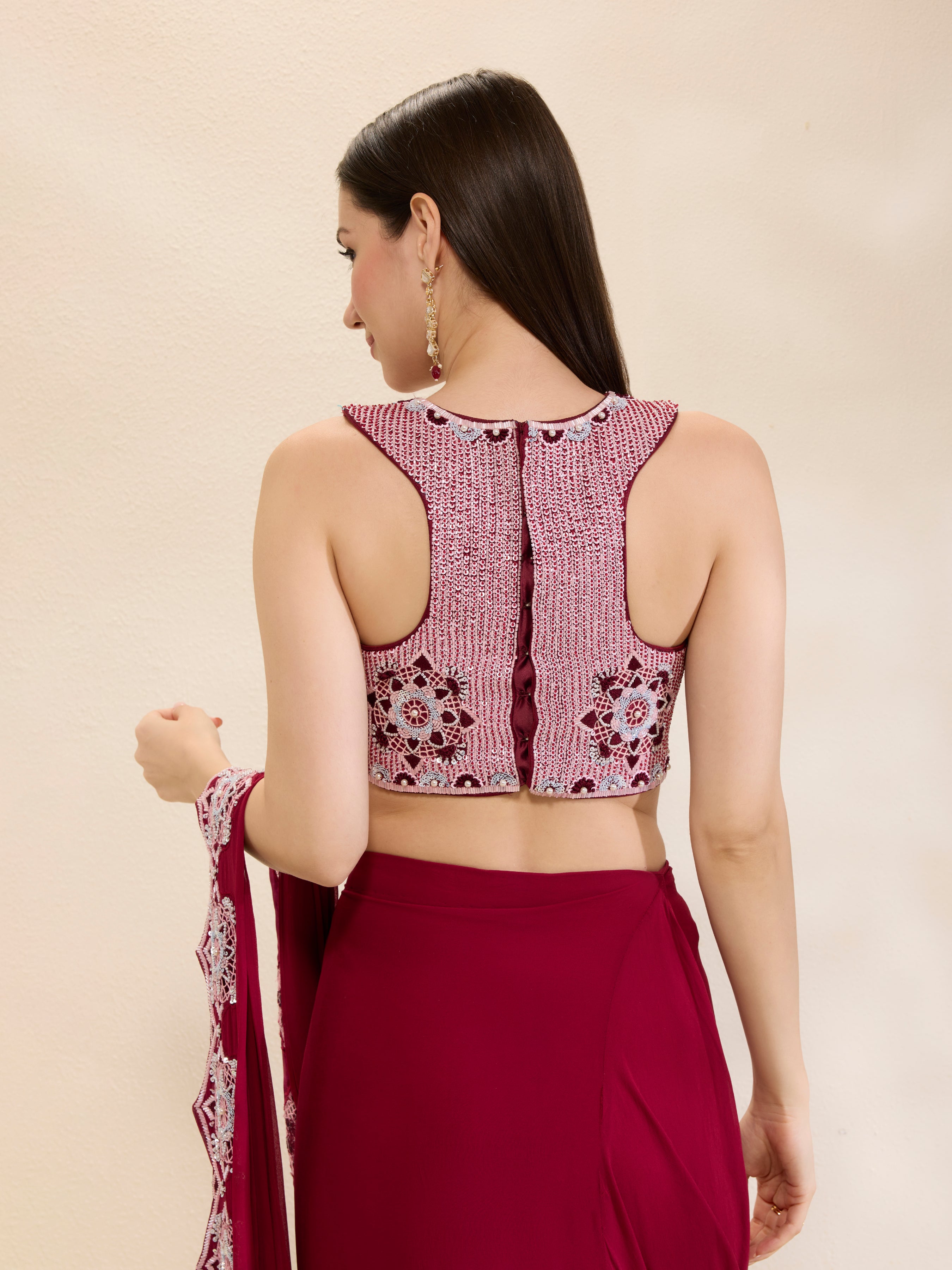 Woman wearing a maroon saree with an embroidered blouse on a beige background