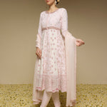 Woman wearing a light pink traditional outfit with a floral pattern on a textured beige background