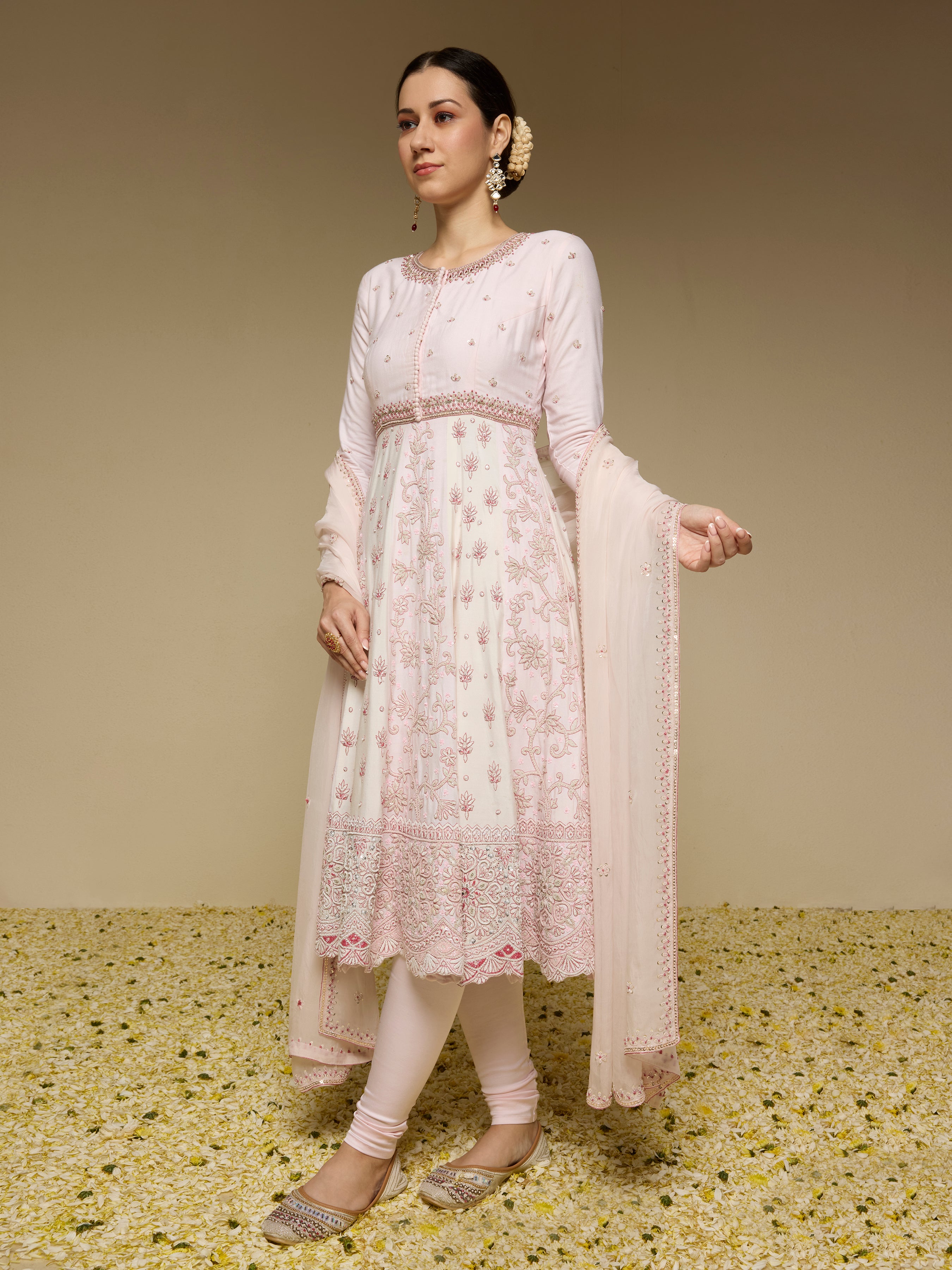 Woman wearing a light pink traditional outfit with a floral pattern on a textured beige background