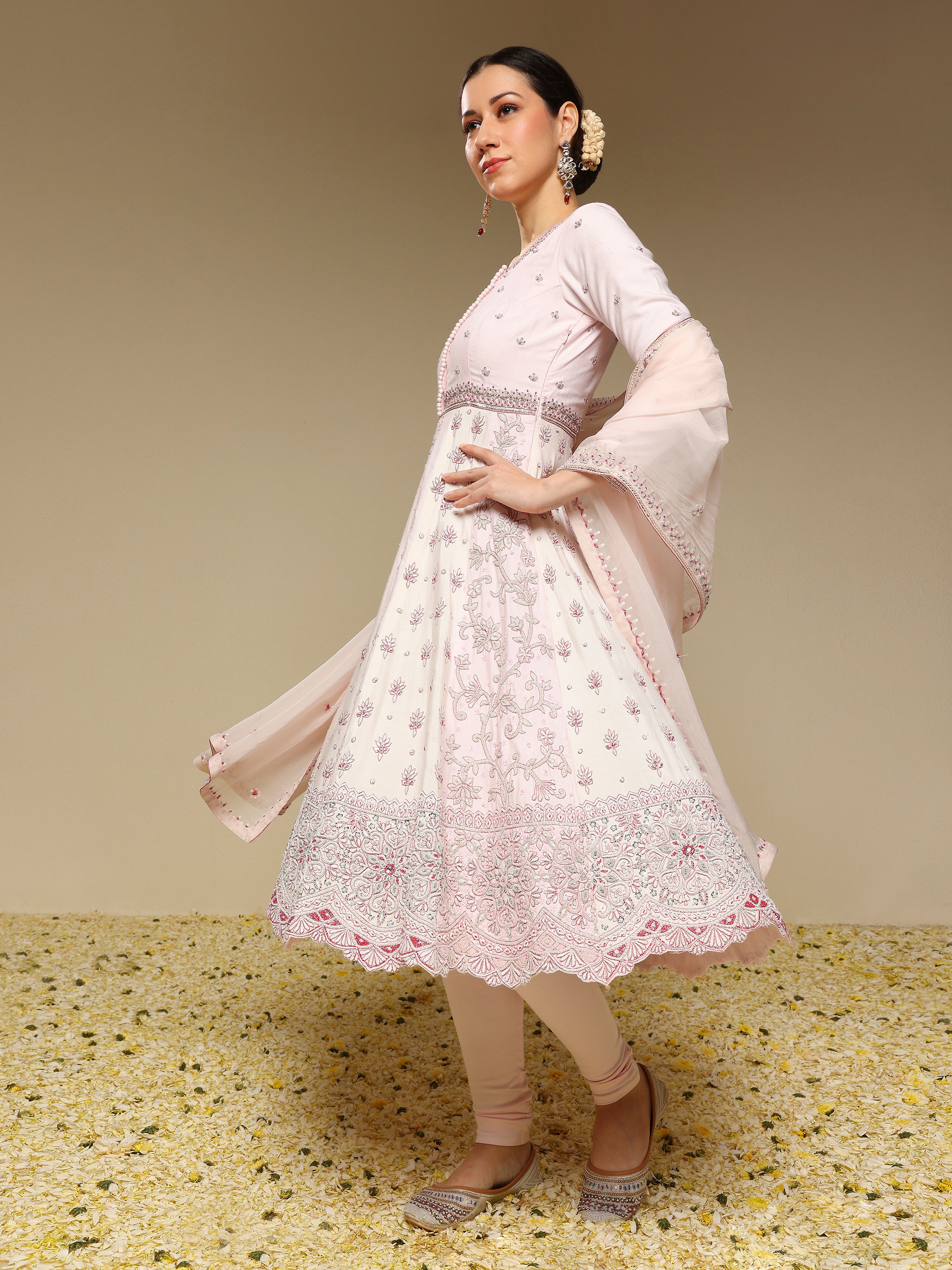 Woman wearing a light pink traditional outfit with floral patterns on a beige background