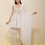 Woman wearing a white embroidered outfit with a sheer dupatta on a beige background