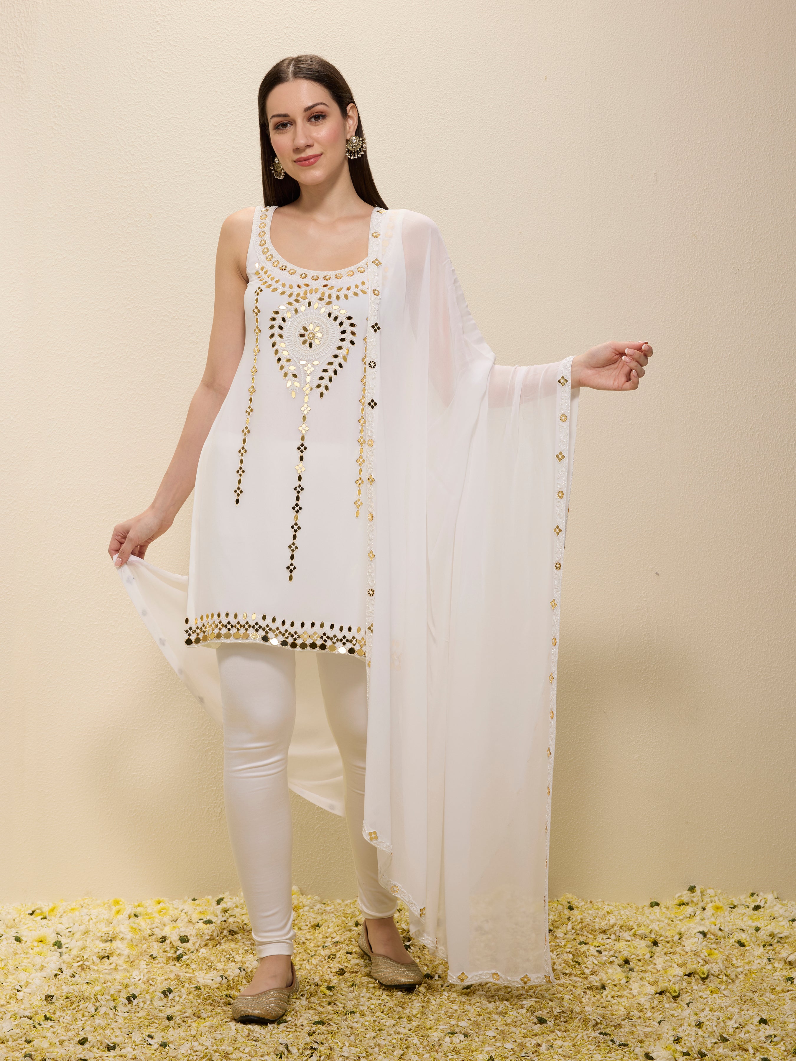 Woman wearing a white embroidered outfit with a sheer dupatta on a beige background