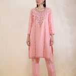 Woman wearing a pink embroidered outfit on a beige background