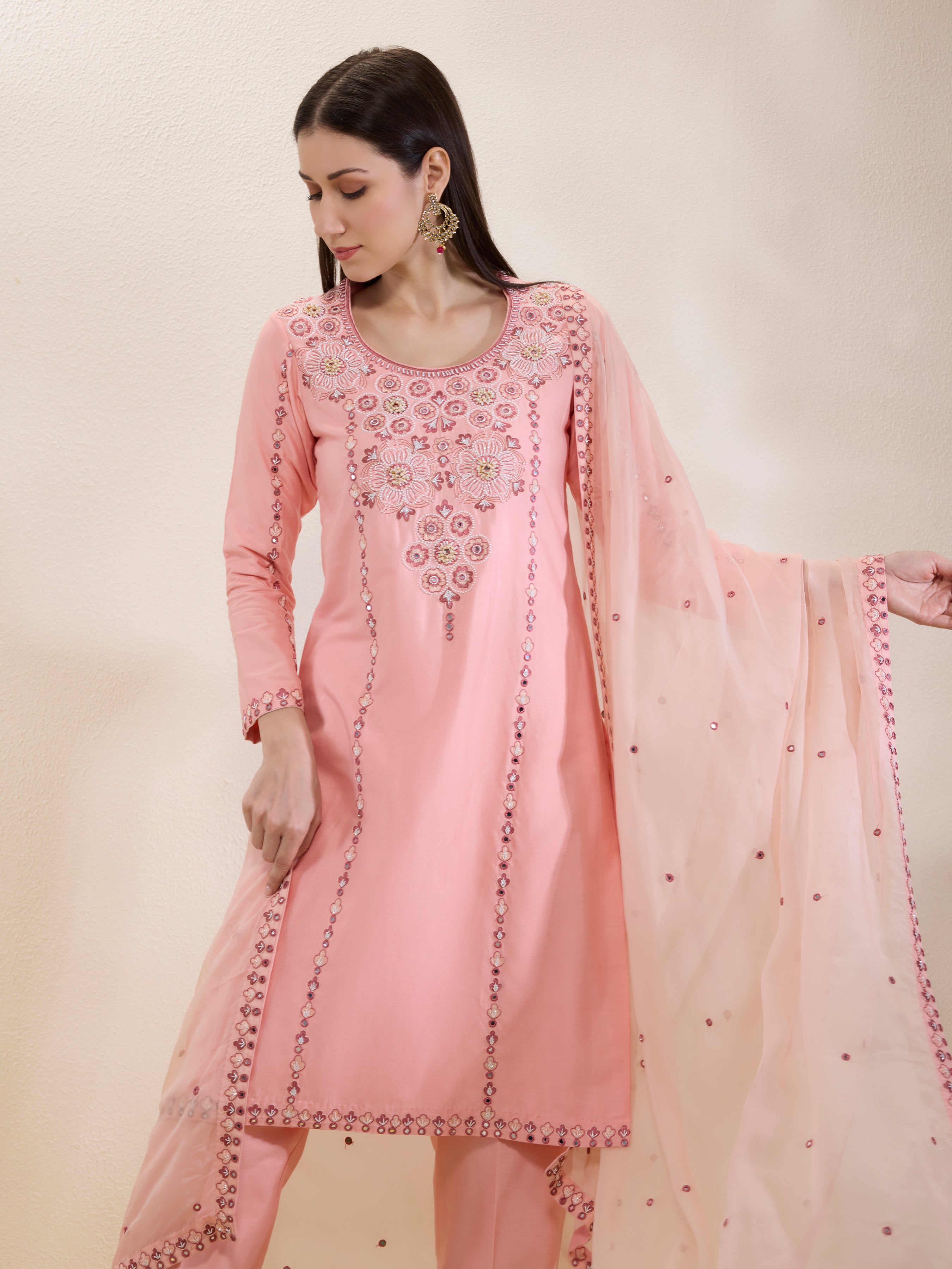 Woman wearing a pink embroidered traditional outfit with a beige background