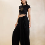 Woman wearing a black crop top and wide-leg pants on a beige background