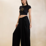Woman wearing a black crop top and wide-leg pants on a beige background