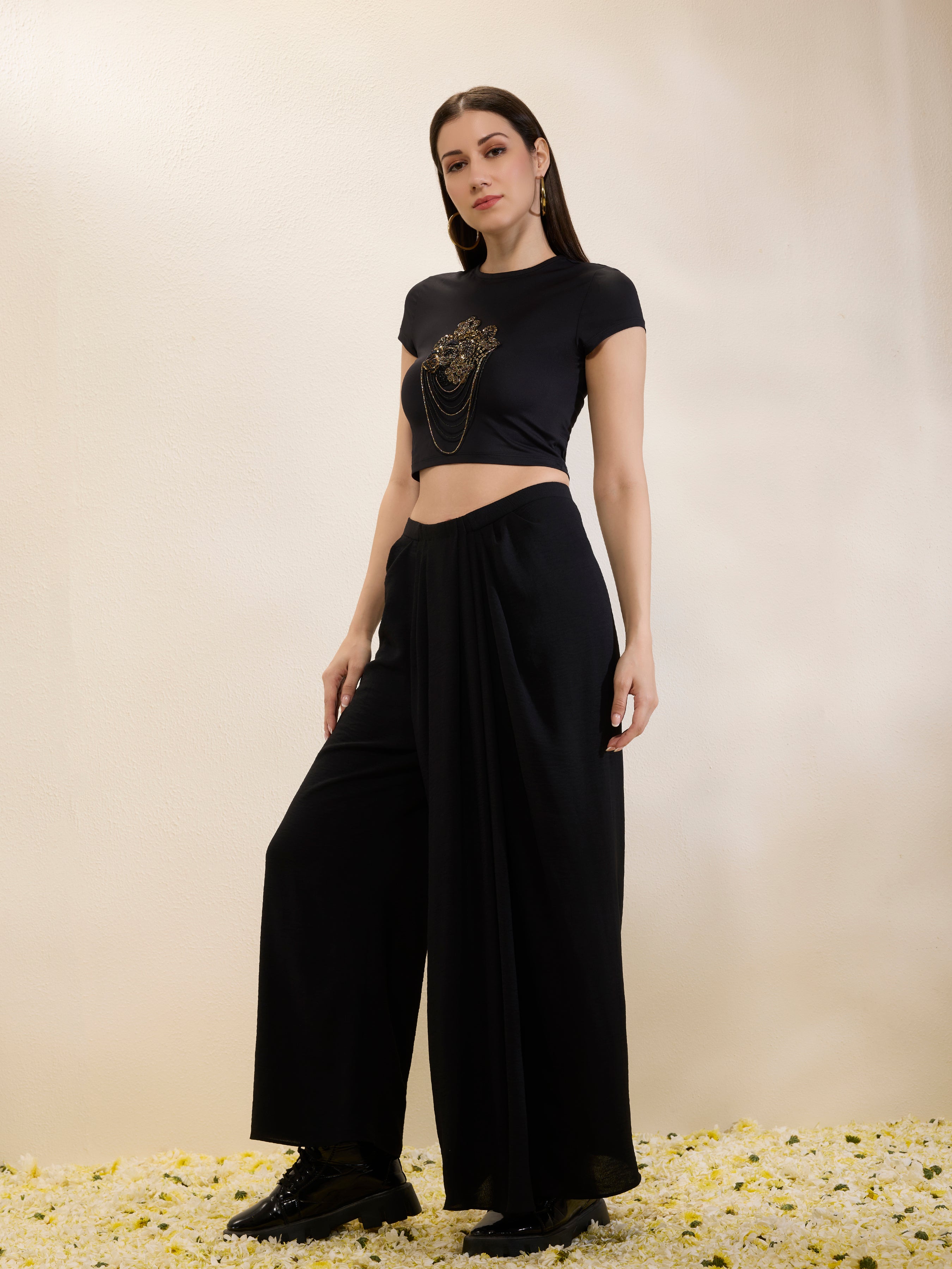 Woman wearing a black crop top and wide-leg pants on a beige background