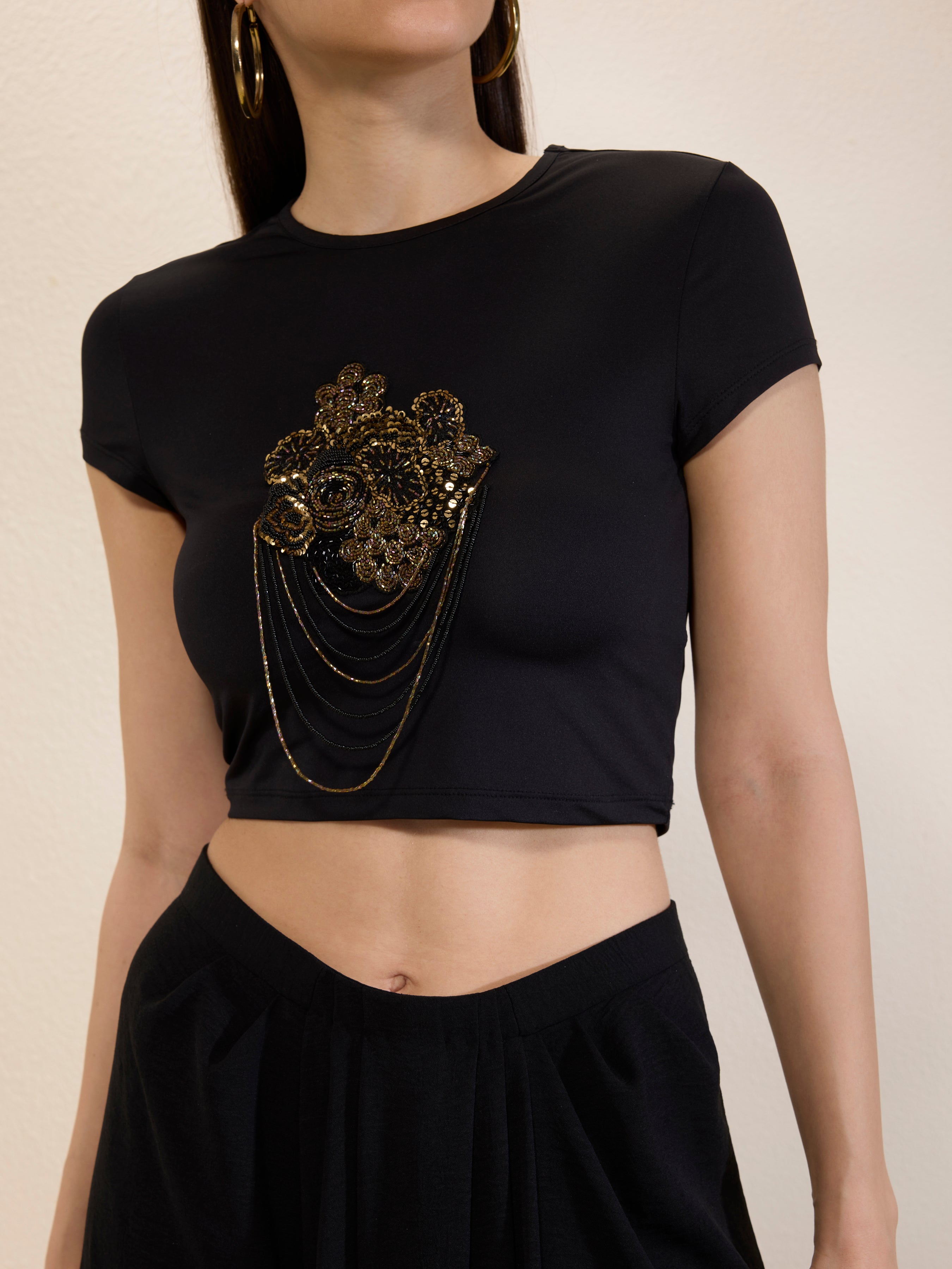 Black crop top with gold embellishments on a neutral background