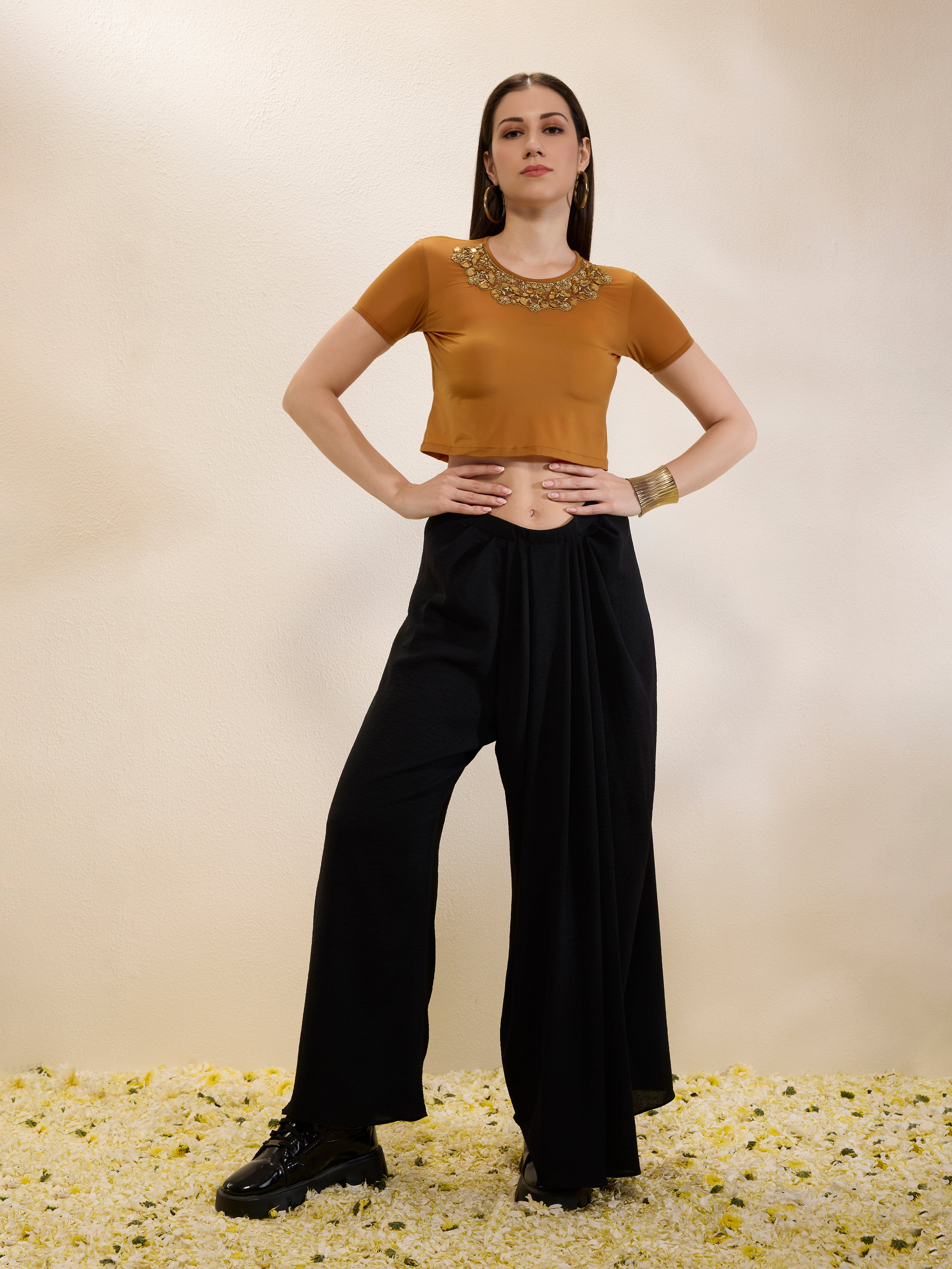 Woman wearing a mustard top and black pants with a gold necklace on a beige background