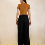 Woman wearing a mustard top and black pants standing on a textured surface with a neutral background
