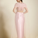 Woman wearing a light pink traditional outfit with a sheer overlay on a neutral background