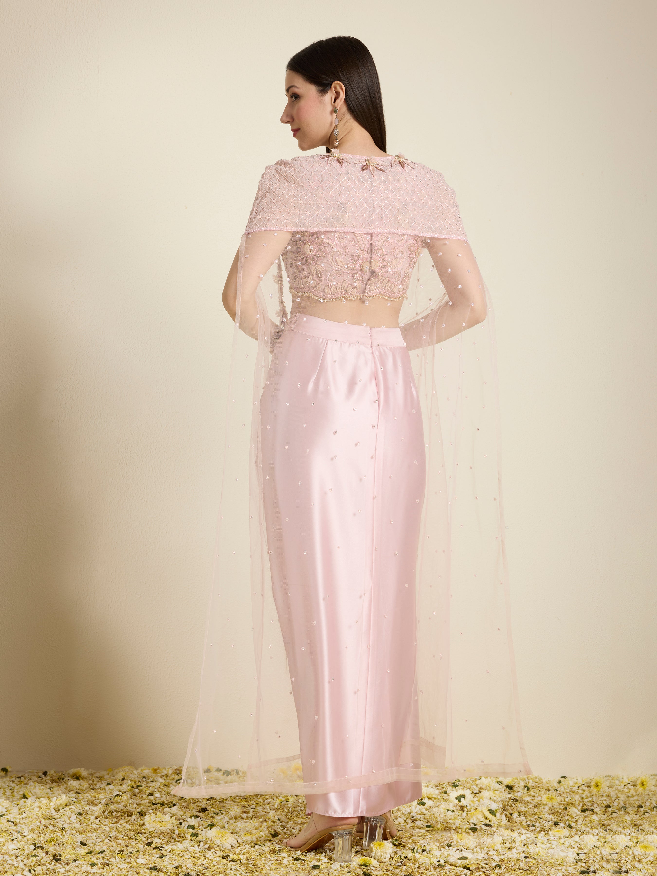 Woman wearing a light pink traditional outfit with a sheer overlay on a neutral background