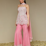 Woman wearing a white lace top and pink pants with a beige background