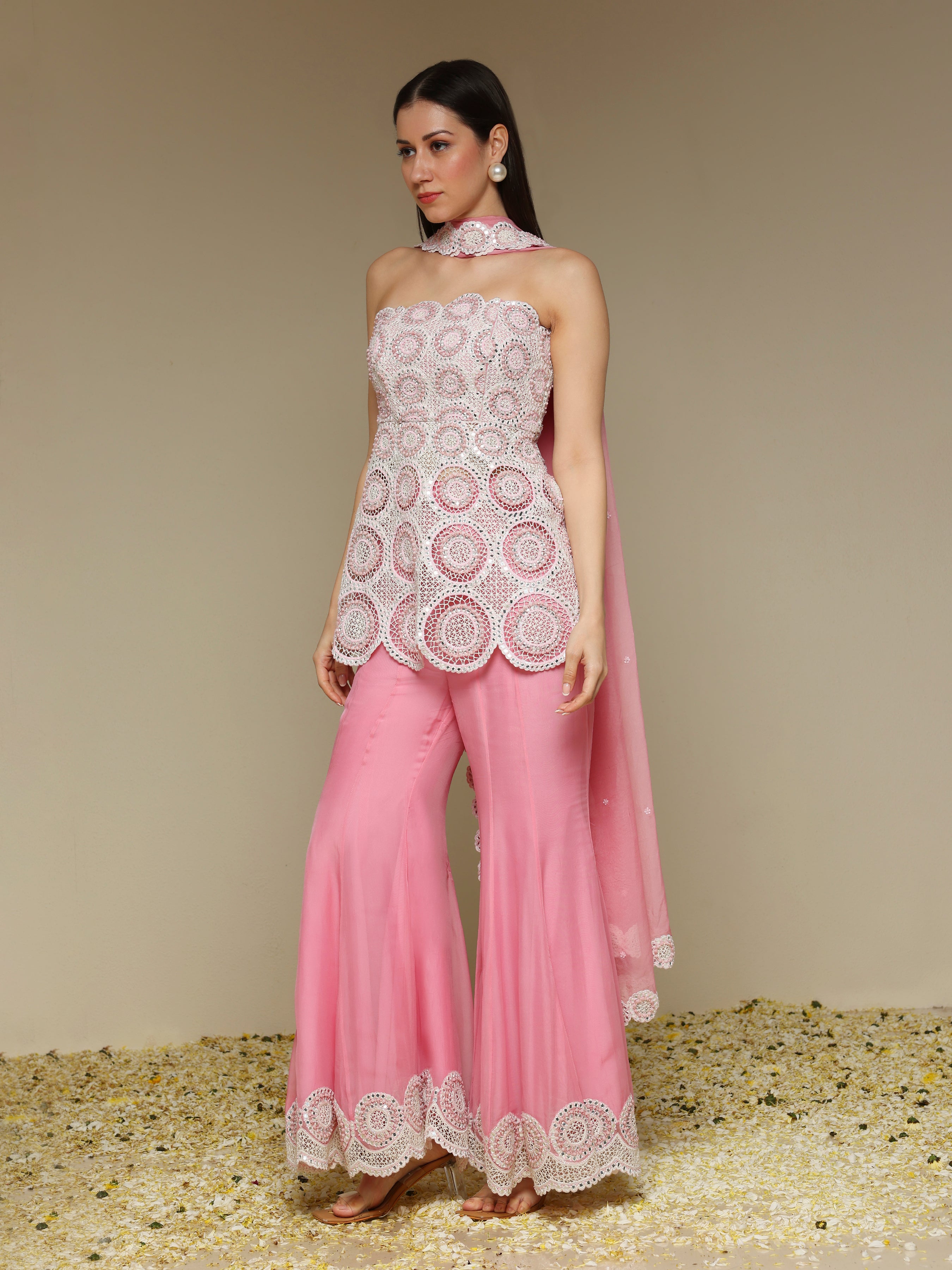 Woman wearing a white lace top and pink pants with a beige background