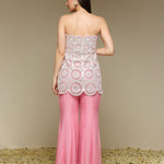 Woman wearing a strapless top and pink pants with lace details on a beige background