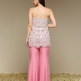 Woman wearing a strapless top and pink pants with lace details on a beige background