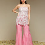 Woman wearing a strapless top and pink pants with lace details against a beige background