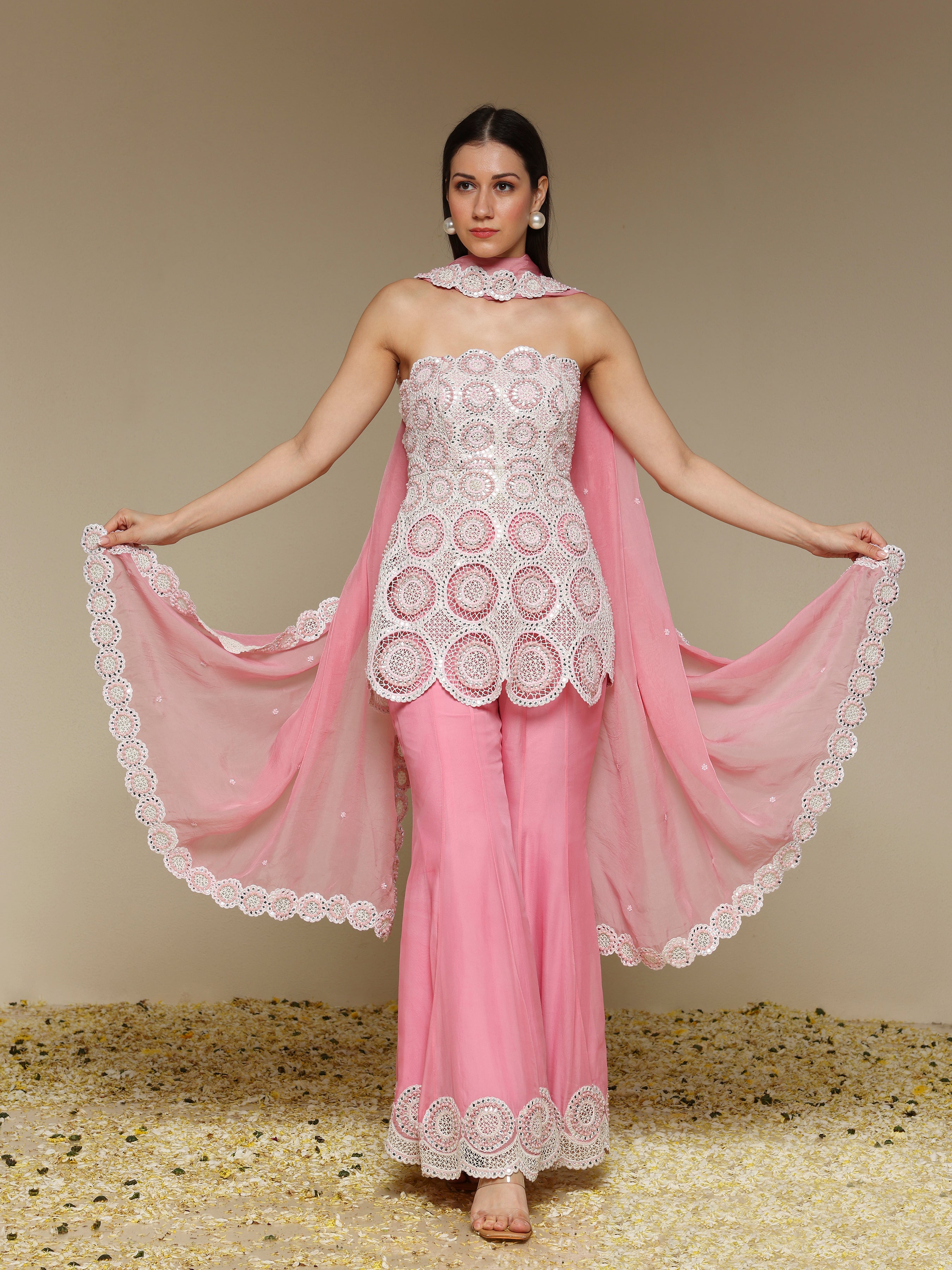 Woman wearing a pink and white outfit with a sheer dupatta against a beige background